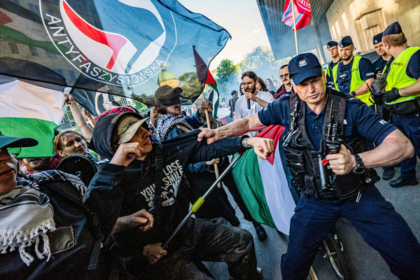 Police tussle with the protesters during the demonstration. Pro-Palestinian protesters gathered at Plac Defilad in Warsaw before marching to the Warsaw Presidential Hotel, where the NexTech Warsaw 2026 technology and security conference was taking place. The event brought together government officials, industry leaders, and defense technology experts, including several current and former Israeli military officers. During the demonstration, some activists lit flares, threw tomatoes at the hotel building, and attempted to enter the venue, leading to confrontations with police.