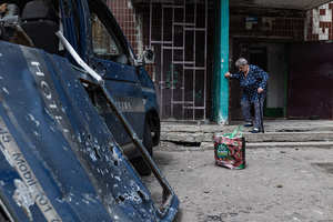 A woman steps out of her house in front of a van damaged by a Russian FPV drone.
