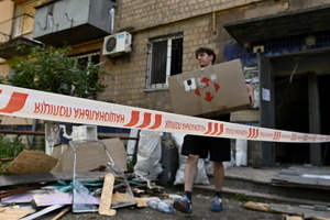 A volunteer carries a box of belongings near a damaged residential building as a result of a missile strike. Following a devastating overnight bombardment in which Russia launched 74 missiles and 496 attack drones, Kyiv has declared July 3, 2026, a city-wide Day of Mourning to honor the victims. At least 25 people were killed and over 80 injured across the capital as direct strikes heavily damaged residential apartment blocks, leaving active search and rescue operations scrambling to locate residents still believed to be trapped under the rubble.