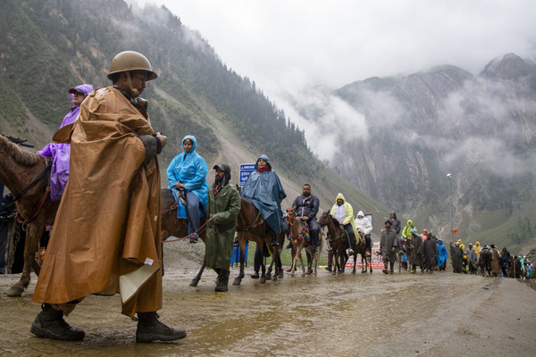 An India paramilitary soldier seen on guard as Hindu devotees make their way on foot, ride horses and are carried by porters along a mountain path during the annual Amarnath pilgrimage to the cave shrine in Baltal some 100 km (62 miles) east of Srinagar. Braving sub-zero temperatures and high-altitude mountain trails, thousands of Hindu devotees have begun the annual Amarnath Yatra pilgrimage across the Himalayas of Indian-administered Kashmir to reach the sacred Amarnath cave, which houses a naturally formed ice stalagmite revered as a symbol of Lord Shiva. Running from July 3 to August 28, 2026, the holy journey is heavily guarded by thousands of security personnel across both the traditional Pahalgam and steeper Baltal routes, even as environmental experts warn that surging crowds and heavy reliance on diesel generators are placing critical pressure on the region's fragile, climate-threatened ecosystem.