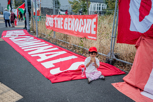 A young child sits alongside a large banner accusing Israel of being war criminals and causing a genocide in Gaza during the rally. Pro-Palestinian protestors gathered outside Elbit Systems factory in Filton, Bristol to accuse the arms company of supplying Israel with weaponry and drones for its war in Gaza.