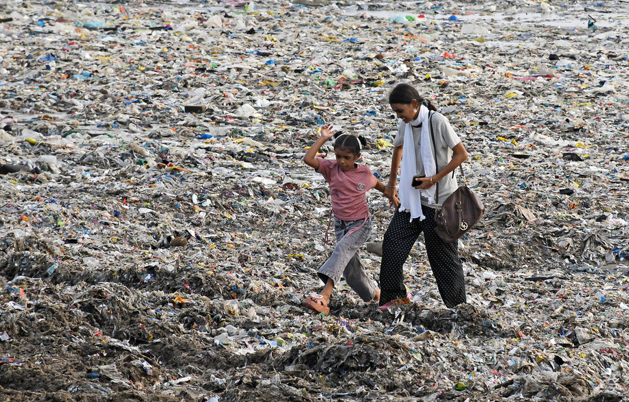 A young girl and a woman walk on a massive amount of garbage washed ashore on Juhu beach. The unprecedented accumulation of massive garbage washed ashore on Juhu beach following a recent high tide has created an unpleasant site and raises a significant concern about city's waste management and drainage system. Large portion of debris enters the Arabian Sea through overflowing storm-water drains and the garbage dumped into Mithi River by slum colonies and small industries on its bank which is washed back onto the coast during heavy rain coinciding with high tide in the sea.