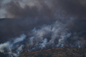 A helicopter flies through a massive column of smoke over Ávila as firefighters battle a wildfire that has prompted an extreme fire danger alert across central Spain, including Madrid and nearby regions.