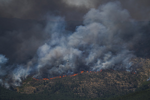 A helicopter flies through a massive column of smoke over Ávila as firefighters battle a wildfire that has prompted an extreme fire danger alert across central Spain, including Madrid and nearby regions.