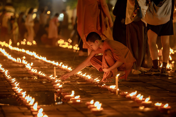 A Buddhist novice monk lights traditional Lanna oil lamps in front of the stupa at Wat Chedi Luang during National Mother's Day celebrations in Chiang Mai.