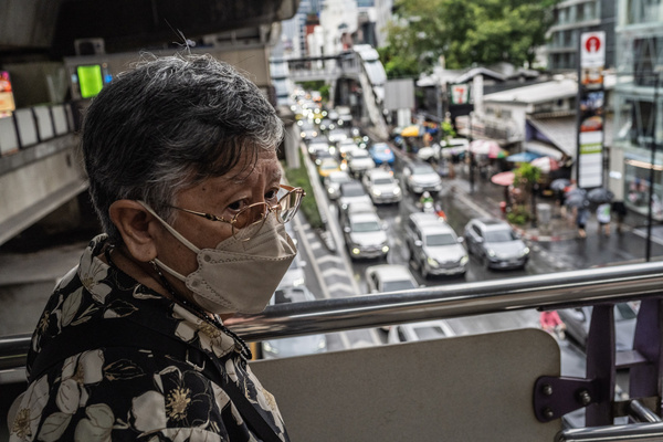 An elderly lady wearing a protective face mask near heavy evening rush hour traffic in central Bangkok.