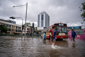 People wade through floodwater beside a bus on Phetchaburi Road. Floodwaters inundate major roads, including Phetchaburi Road and the Pridi Banomyong neighborhood in Bangkok, following a record monsoon downpour that prompted a capital-wide disaster declaration. Municipal pumps operate at full capacity to drain overflowing canals.