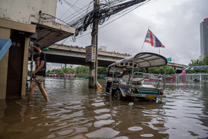 A man walks through floodwater past a parked tuk-tuk near Phetchaburi Road. Floodwaters inundate major roads, including Phetchaburi Road and the Pridi Banomyong neighborhood in Bangkok, following a record monsoon downpour that prompted a capital-wide disaster declaration. Municipal pumps operate at full capacity to drain overflowing canals.