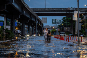 Pedestrians wade through floodwater beneath an elevated road in the Pridi area of Bangkok. Floodwaters inundate major roads, including Phetchaburi Road and the Pridi Banomyong neighborhood in Bangkok, following a record monsoon downpour that prompted a capital-wide disaster declaration. Municipal pumps operate at full capacity to drain overflowing canals.
