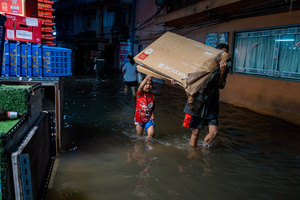 A child and an adult carry a large cardboard box through floodwater in the Pridi area of Bangkok. Floodwaters inundate major roads, including Phetchaburi Road and the Pridi Banomyong neighborhood in Bangkok, following a record monsoon downpour that prompted a capital-wide disaster declaration. Municipal pumps operate at full capacity to drain overflowing canals.