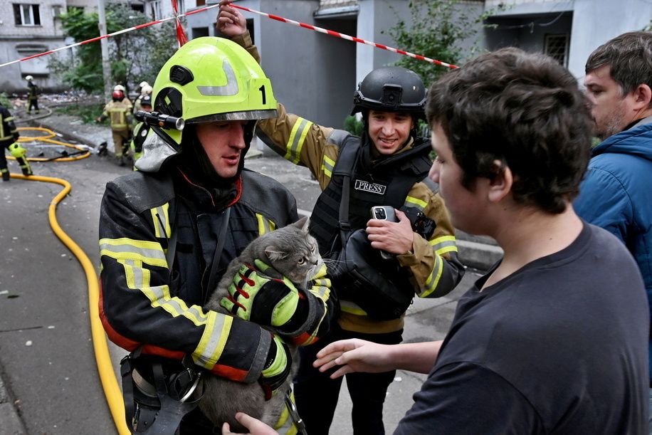 A firefighter hands a rescued cat to its owner at the site where a Russian strike drone hit an apartment building during a Russian attack on the country.