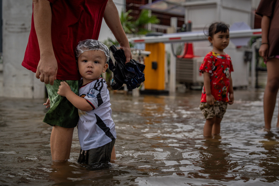 A child holds on to an adult while standing in floodwater near Phetchaburi Road. Floodwaters inundate major roads, including Phetchaburi Road and the Pridi Banomyong neighborhood in Bangkok, following a record monsoon downpour that prompted a capital-wide disaster declaration. Municipal pumps operate at full capacity to drain overflowing canals.