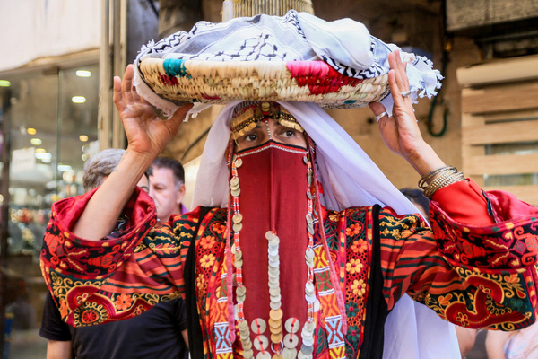 A Palestinian woman, wearing traditional attire adorned with gold jewelry, carries dates to distribute to participants at a bride's "Henna Night" celebration in the Old City of Nablus (West Bank). These rituals are part of the pre-wedding henna ceremonies—a custom observed in many Arab countries, including Palestine, and considered a heritage tradition passed down from ancestors.