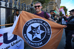 A protester seen holding a flag of pro-Israel lobby group Campaign Against Antisemitism outside the Tower Hamlets town hall during the rally. The 90th anniversary of the Battle of Cable Street is commemorated on Sunday 4 October 2026 in the east end of London. Despite the make-up having changed greatly over the last nine decades, thousands still marched through the streets to oppose Fascism and Zionism. In 1936, over 100,000 Jewish residents, Irish dockers, trade unionists, and local working-class communities stood shoulder to shoulder and repelled Sir Oswald Mosley's British Union of Fascists.