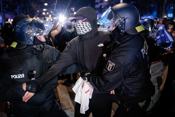 Two police officers wearing protective helmets detain a masked pro-Palestinian protester by the arms during a march in Berlin on the third anniversary of the Hamas-led October 7, 2023 attack on Israel. Assembling at 6:00 p.m. at Oranienplatz, a mobile protest march proceeded through the heart of Berlin's Kreuzberg district under the slogan "Down with Colonialism!" Demonstrators navigated a designated route along Oranienstrasse, Skalitzer Strasse, and Kottbusser Tor before concluding at Hermannplatz. The evening march brought anti-war and anti-colonial messaging into the surrounding neighborhoods, requiring localized traffic diversions and active police monitoring along the corridor.
