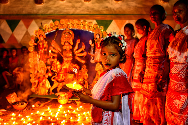 A little girl holding a candle seen in front of the idol of Lord Durga. Durga is a description of the power of the goddess in Hindu Mythology. UNESCO (The United Nations Educational, Scientific and Cultural Organization) in 2021 included Durga puja in the Representative list of the intangible cultural heritage of Humanity.