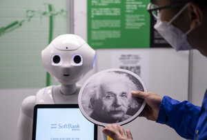 An exhibition staff holds a sign with Albert Einstein headshot  to make the robot recognize human faces at a first glance  during the 'ROBOTS' exhibition at the Hong Kong Science Museum in Hong Kong on May 8, 2021. The exhibition explores the 500-year story of humanoid robots and the artistic and scientific quest to understand what it means to be human.