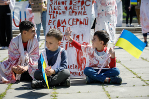 Children with Ukrainian flags sit near a placard on the ground during the performance at the Soviet soldiers cemetery in Warsaw on Victory day. On the 77th anniversary of the Red Army victory over Nazi Germany Ukrainian activists performed at the Soviet soldiers cemetery in Warsaw as they protested against Russian invasion of Ukraine. Activists banned the Russian delegation headed by Sergey Andreev, the Ambassador of the Russian Federation in Poland, from entering the Cemetery. During that attempt diplomats were doused with fake blood by the Ukrainian activists.