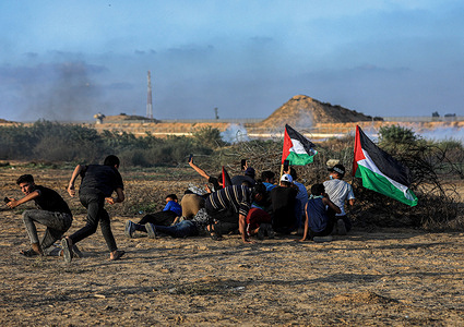 Protesters take cover while holding Palestinian flags during confrontations with Israeli security forces along the border with Israel, east of Khan Yunis, south of the Gaza Strip.