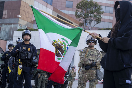 A man holds a flag as law enforcement stand guard outside the Federal Building during a protest. A federal appeals court ruled on June 12 that the Trump administration can maintain control of the California National Guard overturning a lower court ruling that U.S. President Donald Trump's deployment of troops without Governor Gavin Newsom's consent is unlawful.
