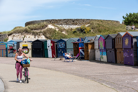 A cyclist pushes her bike front of the nicely decorated beach huts in Westgate-On-Sea. Westgate-On-Sea is a small seaside town in Kent, England. It is a very popular tourist destination.
