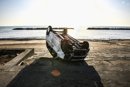 A car seen overturned along the coast after being swept by the tsunami following the Great East Japan Earthquake. Images from Okawa Elementary School and Tokyo Station capture the devastation caused by the March 11, 2011 Tōhoku earthquake and tsunami, as buildings were destroyed, train services halted and families searched through debris for belongings swept away by the tsunami.