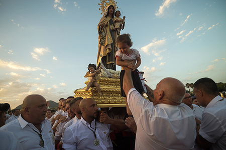 A penitent of 'Virgen del Carmen' brotherhood is seen rising a child in front of the statue of the virgin at the beach as they take part in a procession in 'El Palo' neighborhood. Every year, on 16 July, Malaga City celebrates the 'Virgen del Carmen', the patron of sailors and fishermen. The statue of the Virgin, carried by a group of believers in traditional costume along the streets, is placed on a boat from the beach, which later sails down the Malaga coast.
