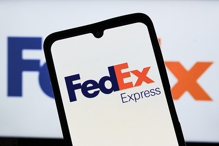 In this photo illustration, the FedEx Corporation logo is displayed on a smartphone screen with a blurred version of the company's branding in the background.