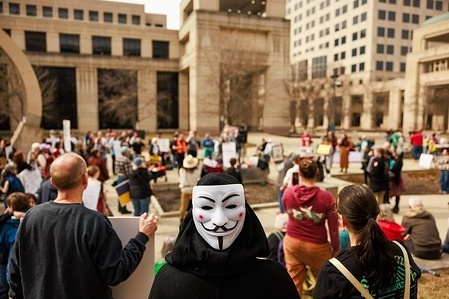 A demonstrator wears a Guy Fawkes mask while protesting against President Donald Trump, Elon Musk, and the Trump administration outside the statehouse. The Democracy demonstration was part of a nationwide call to action by the 50501 Movement which stands for 50 protests, 50 states and one day.