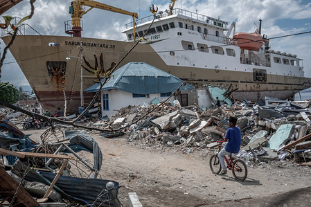 A local seen riding a bicycle next to a stranded ship.
A deadly earthquake measuring 7.5 magnitude and the tsunami wave caused by it has destroyed the city of Palu and much of the area in Central Sulawesi. According to the officials, death toll from devastating quake and tsunami rises to 1,480, around 800 people in hospitals are seriously injured and some 62,000 people have been displaced in 24 camps around the region.