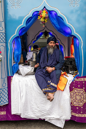 Barefoot Sikh man seen seated in a decorated place during Vaisakhi, a day of profound significance in the Sikh calendar. Some participants carry ceremonial swords as symbols of faith, while others walk barefoot and gently brush the route ahead, reflecting humility, devotion, and respect as the community celebrates its cultural heritage and raises awareness of key social and humanitarian issues.