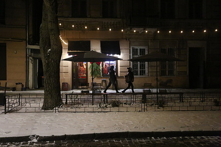 People walk past a generator-powered cafe on snow-covered Pavla Zeleny Street. The power situation in Odessa remains challenging. Power outage schedules are in effect. Prime Minister Yuliia Svyrydenko has instructed regional military administrations and local governments to reduce electricity consumption by eliminating decorative lights and street advertising. Lighting for roads with a high accident rate remains a priority, and the energy-saving measures do not apply to on-site generation.