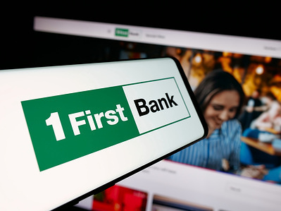 In this photo illustration, a smartphone with the logo of financial company First BanCorp (FirstBank) is seen on screen in front of website.