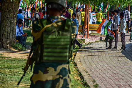A student holds an Indian National Flag as a paramilitary trooper stands alert during a rehearsal of the Tri-colour or Tiranga rally ahead of India's 79th Independence Day on August 15, 2025 in Ganderbal.