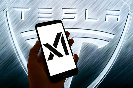 In this photo illustration, the artificial intelligence company xAI logo is seen displayed on a smartphone with a Tesla logo in the background.