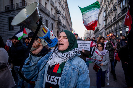 A protester wearing a keffiyeh around her neck shouts slogans through a megaphone during a demonstration through the streets of Madrid, in support of the Palestinian people, in commemoration of Palestinian Land Day.