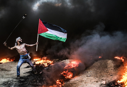 Palestinian protester seen holding a flag while using a slingshot to hurl stones during the clashes following a demonstration near the border with Israel.