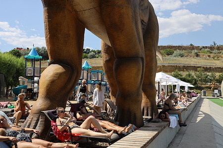 People are seen relaxing in the shade of an Apatosaurus dinosaur figure, part of a tourist attraction at the beach in the village of Fontanka. Despite the ongoing military aggression of the Russian Federation, Ukrainians take vacations and leisure on the Black Sea coast.