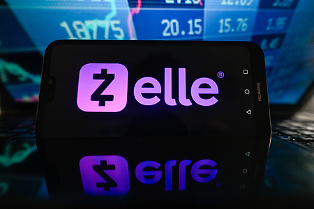 In this photo illustration, a Zelle logo is displayed on a smartphone with stock market percentages in the background.