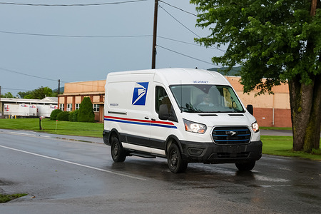 A United States Postal Service (USPS) worker drives a USPS delivery vehicle.