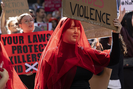 A protestor holds a placard condemning gender-based violence whilst wearing a red veil. Protestors marched in Melbourne on the eve of Mother's Day in Australia to protest violence against women and domestic violence.