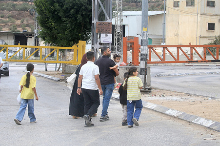 A family seen passing by an iron gate closed off by the Israeli army. The Israeli army enforced a general lockdown across the West Bank, closing border crossings and locking permanent iron gates at the entrances of Palestinian towns under Palestinian Authority administration. Official sources confirmed that the military barriers, secondary road closures, and tightened checkpoint inspections will remain active through the Feast of Tabernacles (Sukkot) until October 3. The holiday closure coincides with intensified security operations and raids by Israeli forces across regional governorates to restrict transit between Palestinian municipalities.