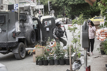 A Palestinian woman walks past an Israeli soldier in the middle of a market during a military raid. Israeli army forces stormed the central market and clashes erupted between Palestinian youths and army forces. The Red Crescent reported that approximately 44 Palestinian youths were injured and one youth was arrested during the military operation.