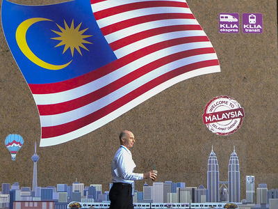 A foreigner is seen with a Malaysia flag as a background.

Kuala Lumpur or commonly known as KL is the national capital for Malaysia and is the fastest growing metropolitan regions in South-East Asia. The urban city is also well known to the world for tourism and shopping. Kuala Lumpur has a great public transportation for people travel around the city.