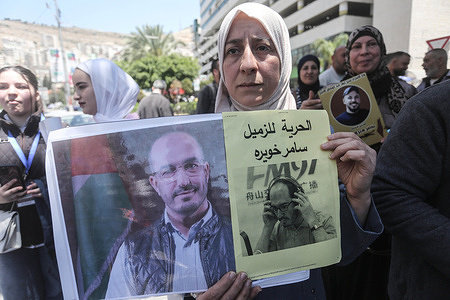 The mother of a Palestinian journalist holds up pictures of her imprisoned son during a protest demanding the release of Palestinian prisoners in Israeli jails.