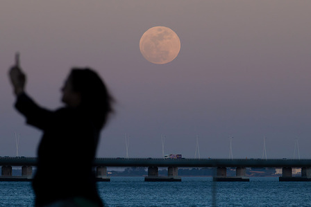A silhouette of a person taking a selfie seen as the full moon rises over the skies near the Tejo River and the Vasco da Gama Bridge. The Pink Moon as it is known marks the beginning of spring in the Northern Hemisphere and the blooming of some wild plants.
