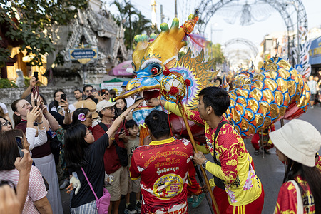 A woman places money into the mouth of a dragon figure during a dragon dance performance along Tha Phae Road in Chiang Mai as part of Chinese New Year celebrations. Residents and tourists gather around the colorful dragon head, taking photographs and participating in the Lunar New Year festivities.