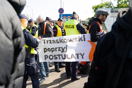 Climate activists sit behind a banner in that says "Trzaskowski support the demands" in Polish. On May 6 2025 climate activists from the group Ostatnie Pokolenie (The Last Generation) staged a road blockade on Słomińskiego Street disrupting access to Gdański Bridge. Eleven individuals participated in the peaceful protest by sitting on the roadway and holding banners. The action was part of an ongoing campaign calling for affordable and accessible public transport as a step toward climate justice. Police officers were present at the site and traffic was rerouted. This marked the second consecutive day of such demonstrations in the Polish capital.