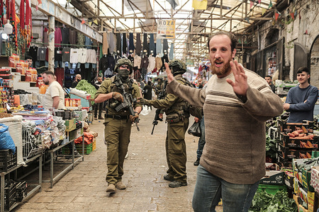 A Palestinian walks past Israeli soldiers in the center of the Old City market in Nablus during a security operation. Israeli forces raided the market, targeting shops. Dozens of Palestinians were arrested in West Bank cities under the control of the Palestinian Authority, headed by President Mahmoud Abbas.