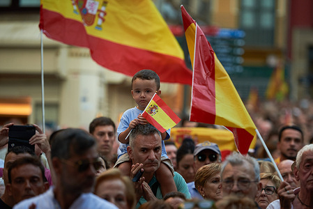 A child on his father's shoulders seen holding a Spanish flag at the demonstration. Tens of thousands of people gathered, turning the annual Ceuta Day holiday into a protest across Spain including in Pamplona, over Prime Minister Pedro Sánchez's handling of a migration crisis in Ceuta. The demonstrations followed a late-July border breach in which more than 72,000 migrants crossed from Morocco, with thousands remaining in the city and pressure mounting on local services. Opposition parties supported the protests and called for stronger border controls, while Sánchez's government defended its response and blamed disinformation for worsening the crisis.